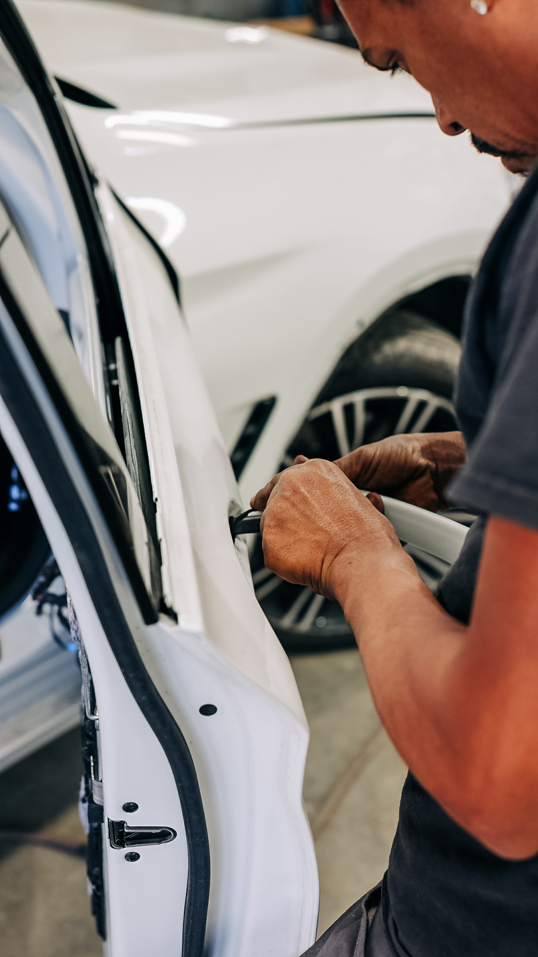 Technician performing dent repair on white vehicle door panel at Quality Auto Body in Fairfax, VA